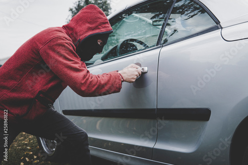 Bilde på lerret Criminal in black balaclava and hoodie opens somebody's vehicle with skeleton key