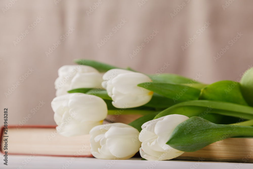 Beautiful composition with white tulips and old books on a beige blurred background in the morning light. Spring reading