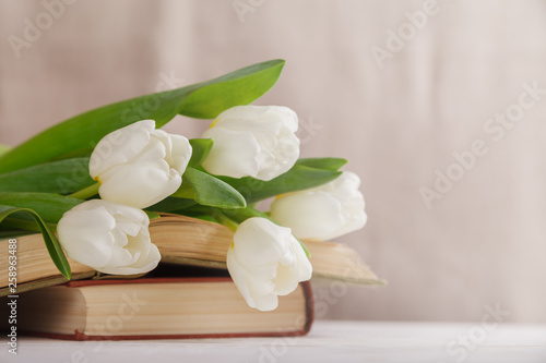 Beautiful composition with white tulips and old books on a beige blurred background in the morning light. Spring reading