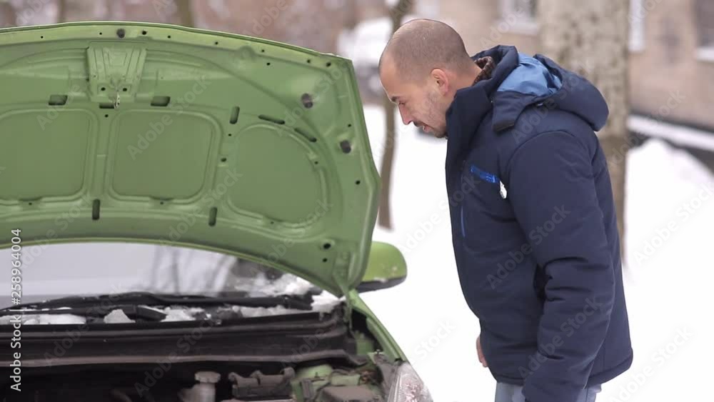 broken car. the man does not know what to do picking under the hood. winter broken car. the man does not know what to do picking under the hood. winter