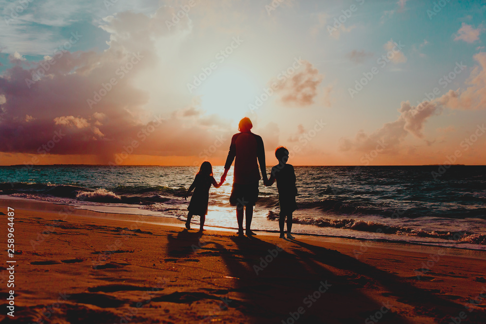 Fototapeta premium father with two kids walking on beach at sunset