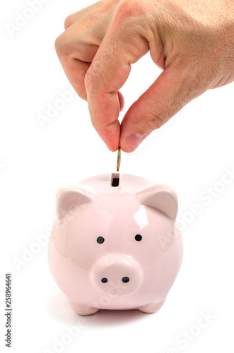 Man hand puts a coin in a pink piggy Bank.