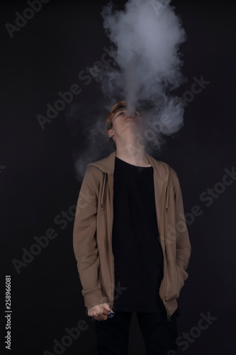 young man smokes, smokes, poses on black background