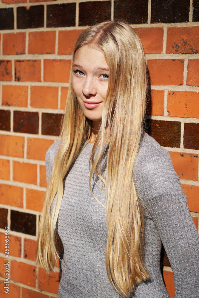teenage girl with long blond hair leaning against brick wall teenage girl with long blond hair leaning against brick wall