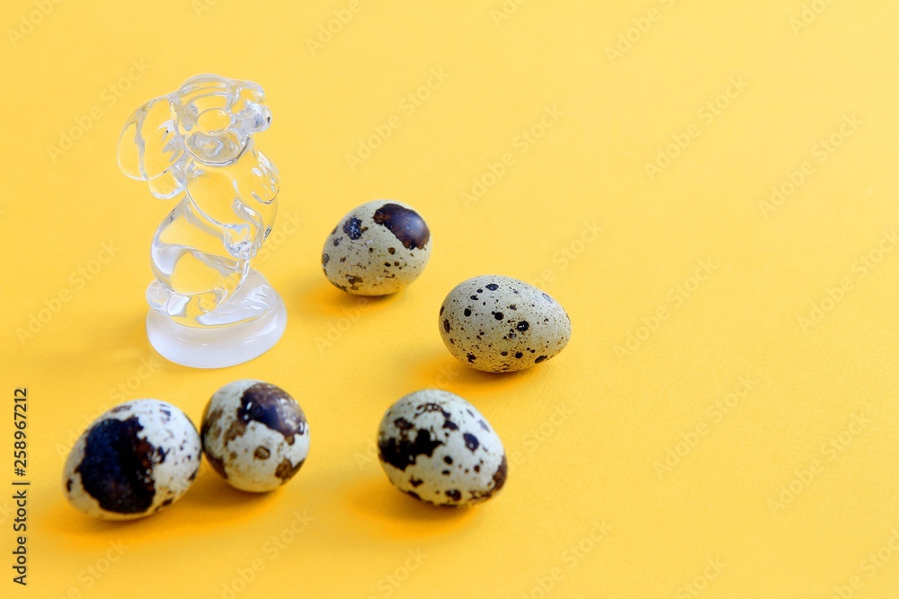 five speckled quail eggs and a rabbit figurine made of transparent glass on a yellow background Easter concept five speckled quail eggs and a rabbit figurine made of transparent glass on a yellow background Easter concept