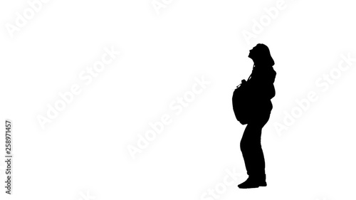 Woman with a backpack pulls out a cap and puts. Silhouette. White background. Side view photo