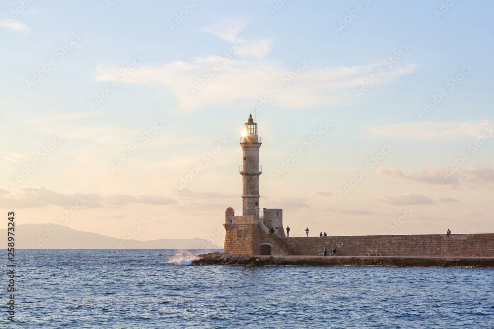 The lamps light up the lighthouse at the evening time. Ancient architecture. The location of the seaport Chania, Creete island, Greece. Sunset. Landscape with the mountains and the sea.