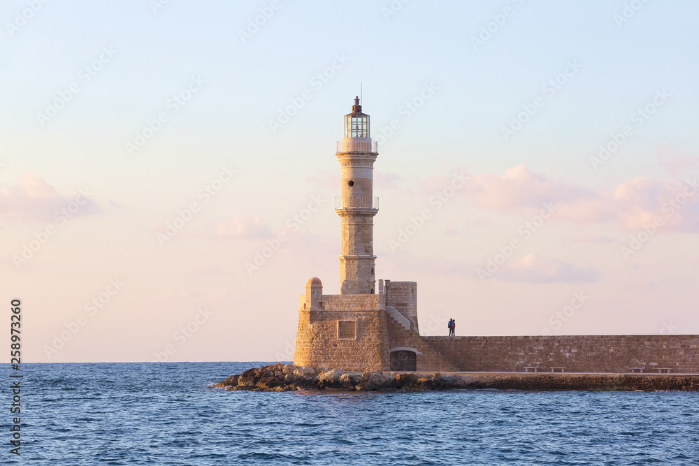 Scenery with beautiful ancient lighthouse surrounded by the sea. Sunset sky with pink light. High mountains. Location is the seaport Chania, Creete island, Greece.
