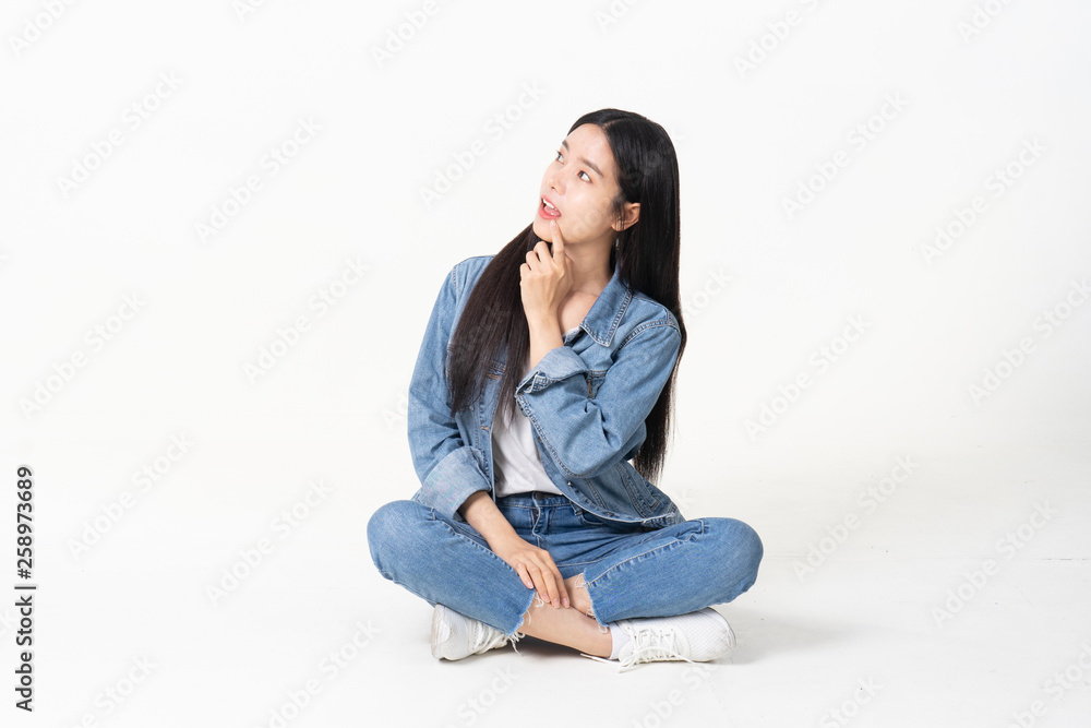 Thinking asian woman sitting on floor isolated on white background.Asian female model smiling looking up.woman pointing fingers away while sitting on a floor with legs crossed isolated