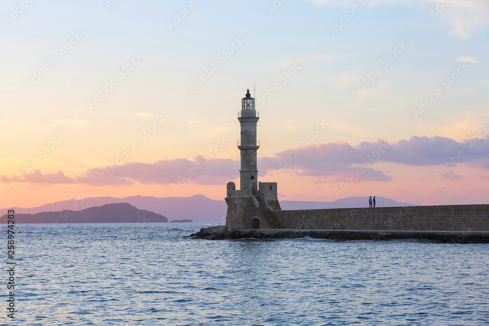 Scenery with beautiful ancient lighthouse surrounded by the sea. Sunset sky with pink light. High mountains. Location is the seaport Chania, Creete island, Greece. Scenery with beautiful ancient lighthouse surrounded by the sea. Sunset sky with pink light. High mountains. Location is the seaport Chania, Creete island, Greece.