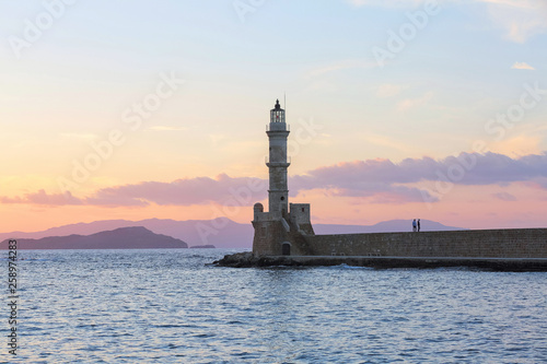 Scenery with beautiful ancient lighthouse surrounded by the sea. Sunset sky with pink light. High mountains. Location is the seaport Chania, Creete island, Greece.
