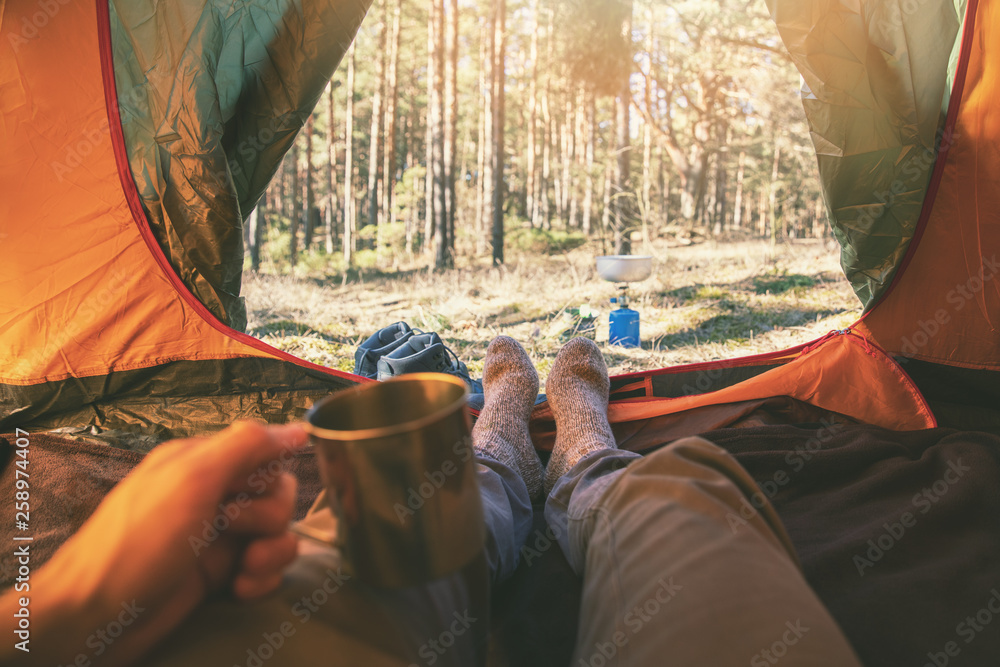 outdoor tourism - man laying in tent with cup of tea - obrazy, fototapety, plakaty 