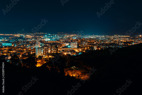 Night view from over capital of Georgia, Tbilisi. Street lights and hills surrounding the city. Blue sky. - Image