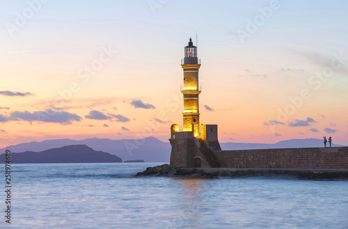 The lamps light up the lighthouse at the evening time. Ancient architecture. The location of the seaport Chania, Creete island, Greece. Sunset. Landscape with the mountains and the sea.