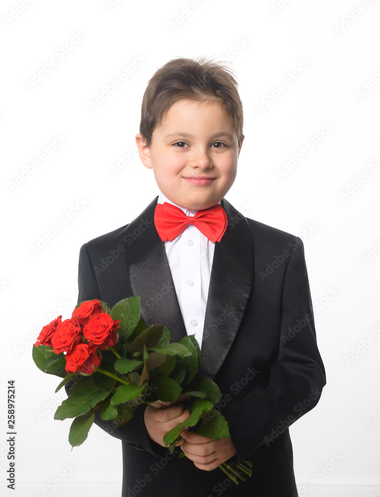 A young boy in a black suit with a red bow tie holding a bouquet of roses A young boy in a black suit with a red bow tie holding a bouquet of roses
