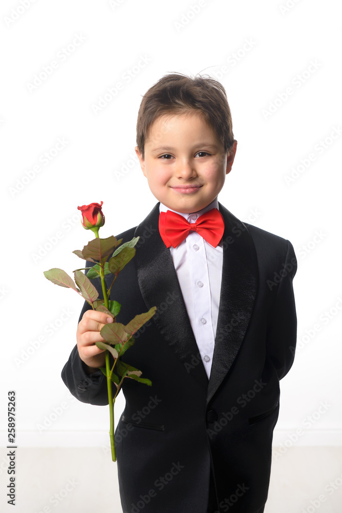 A young boy in a black suit with a red bow tie holding a bouquet of roses A young boy in a black suit with a red bow tie holding a bouquet of roses