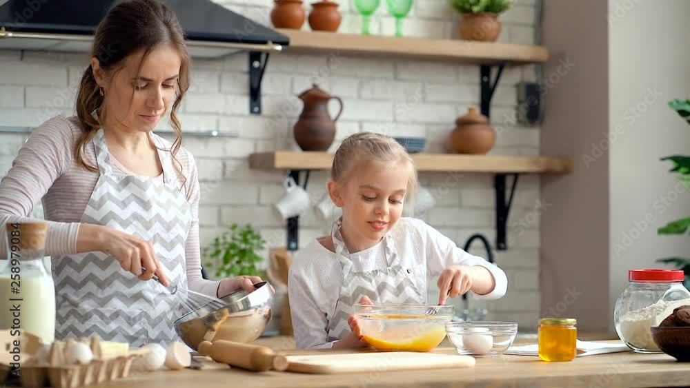 Happy, smiling mother and daughter preparing dough together. Mixing dough in the bowls. Happy, smiling mother and daughter preparing dough together. Mixing dough in the bowls.