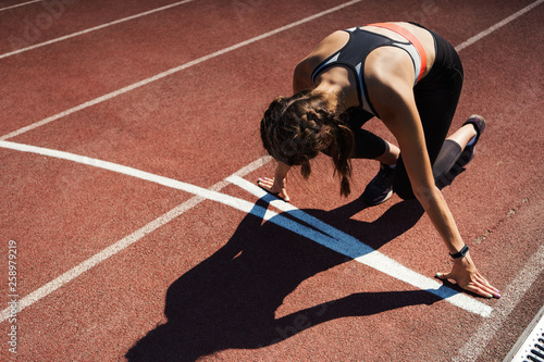 Fototapeta Naklejka Na Ścianę i Meble -  From above view of teen girl in sportswear with smartwatch on her wrist ready to start running on track at stadium