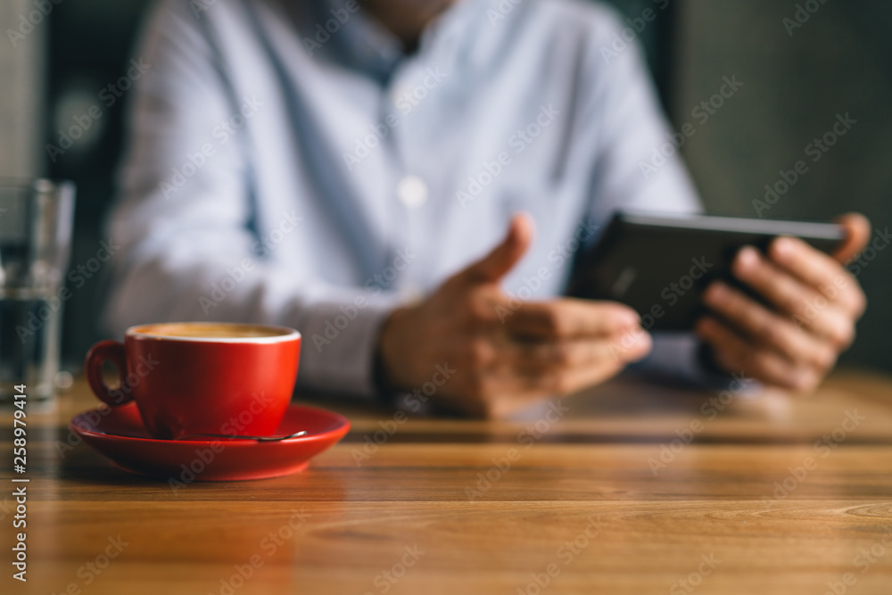 closeup of cup of coffee and blurred man using tablet in background closeup of cup of coffee and blurred man using tablet in background