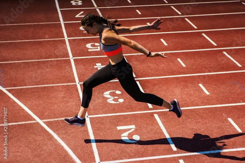 Obraz Boczny widok żeńska nastoletnia atleta w sporta staniku i rajstopy pomyślnie kończy rasy na śladzie przy stadium