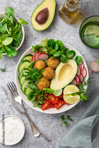 healthy vegan lunch bowl salad with avocado, falafel,cucumber, tomato and redish, top view
