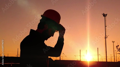 Sagoma di un ingegnere edile e civile mentre indossa il caschetto di sicurezza visto di profilo. Scena al rallentatore al tramonto. photo