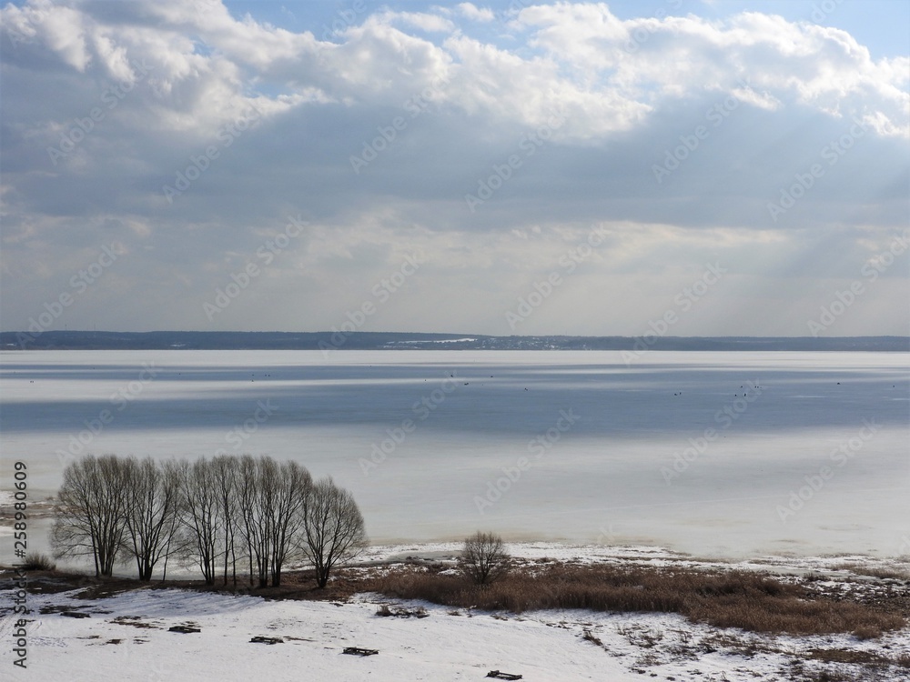 Ice frozen lake on a Sunny winter day in Russia. White snow and clouds in the blue sky. Beautiful winter landscape.