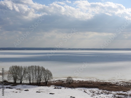 Ice frozen lake on a Sunny winter day in Russia. White snow and clouds in the blue sky. Beautiful winter landscape.