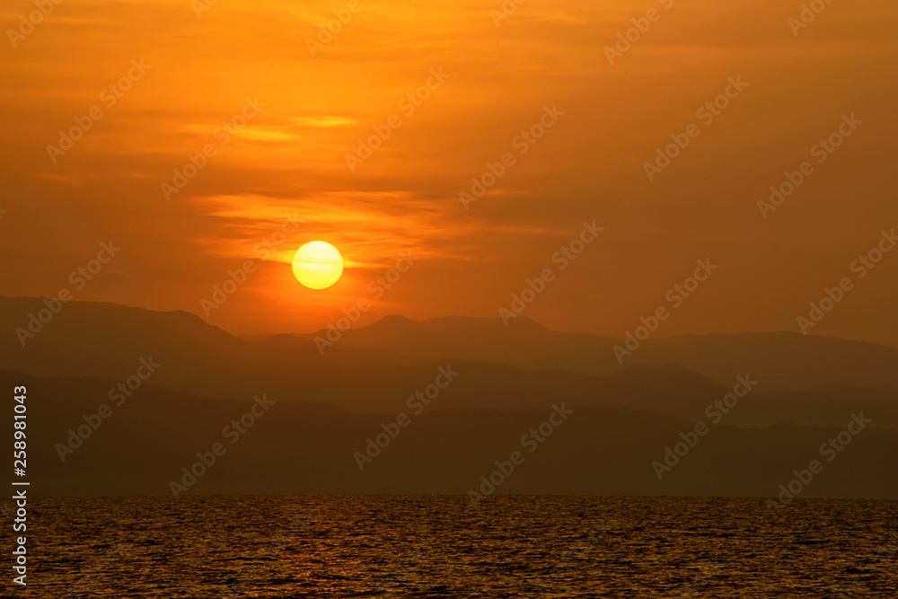 Golden light of sunrise behind the mountains and the sea.