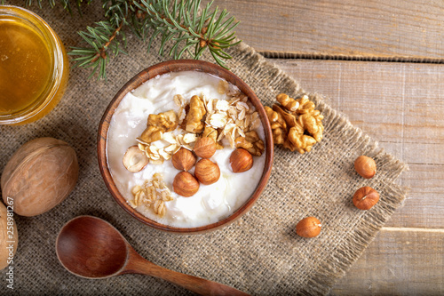 Wooden bowl with yogurt with rolled oats and nuts on burlap napkin on wooden table.