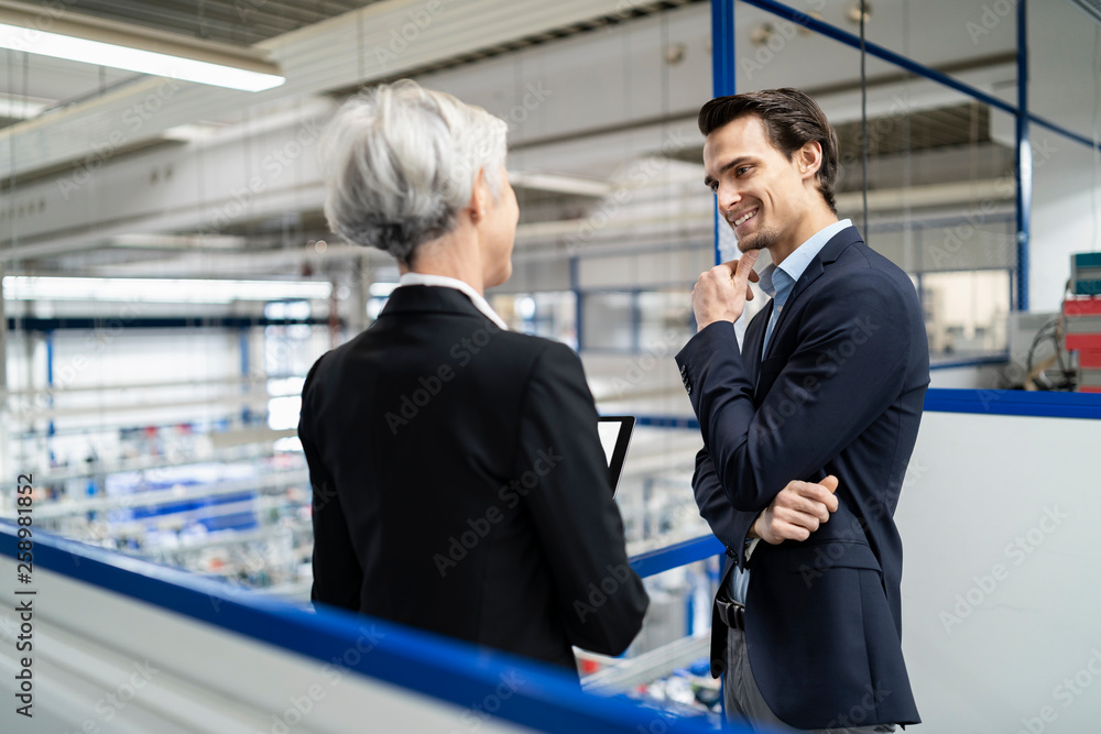 Smiling businessman and senior businesswoman with tablet talking in a factory Smiling businessman and senior businesswoman with tablet talking in a factory