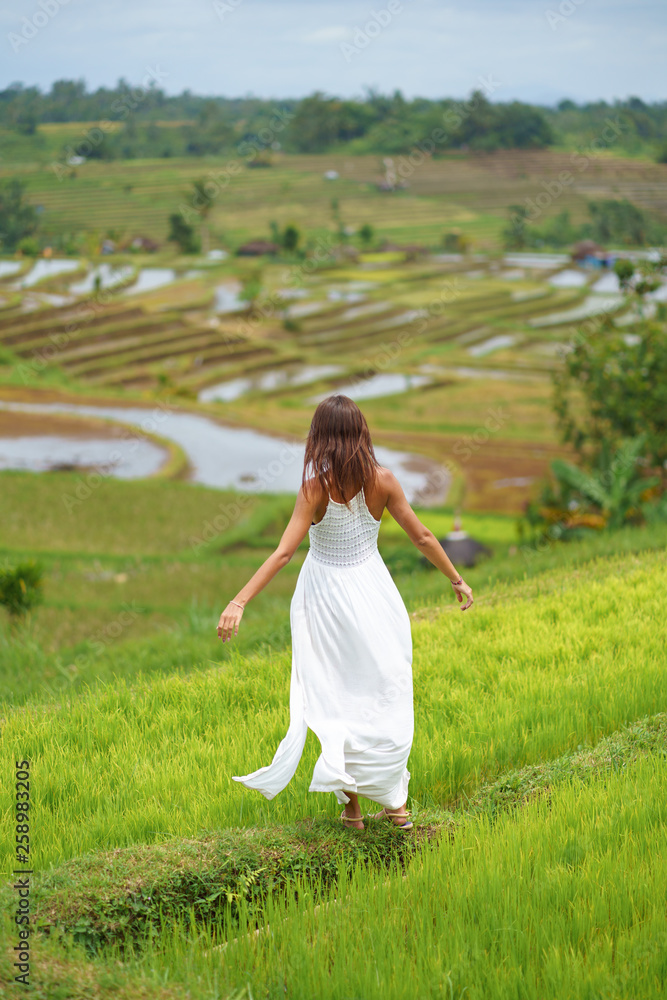 A young woman with her arms outstretched posing standing on a hill. In the background are rice fields
