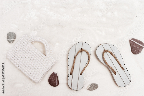 Womens summer traveler accessories, white knitted bag and sandals on white sand background. Concept of travel. Summer background
