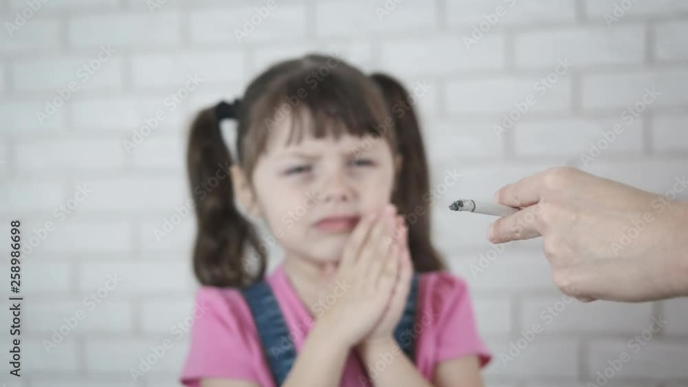 Cigarettes and child. Parents smoke in front of the child. The little girl is choking on the cigarette smoke. Cigarettes and child. Parents smoke in front of the child. The little girl is choking on the cigarette smoke.
