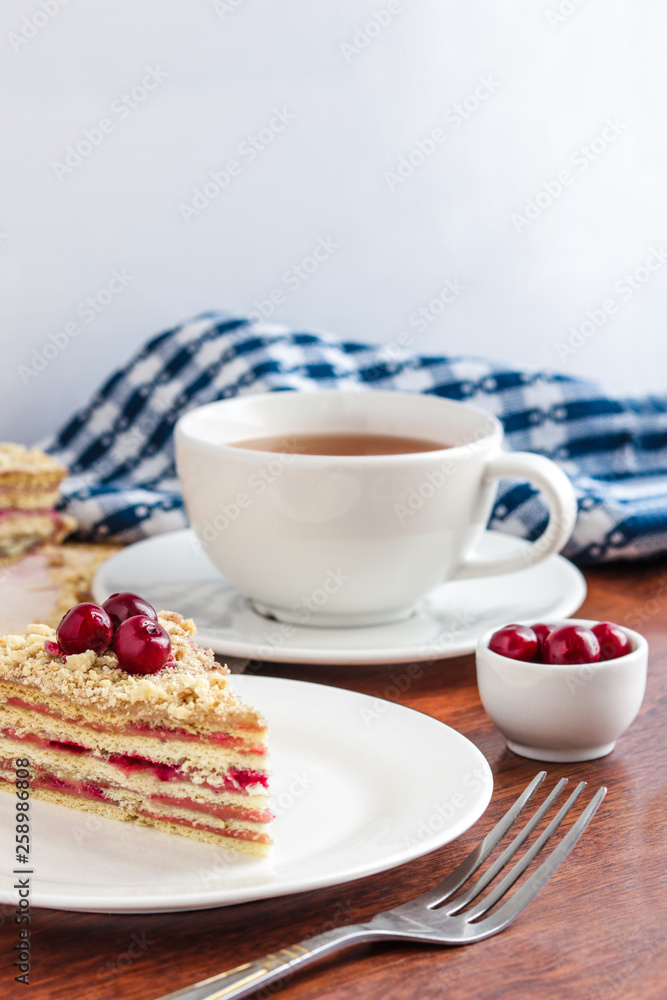 piece of cake on the plate cup of tea cherry in small bowl napkin vertical composition soft focus piece of cake on the plate cup of tea cherry in small bowl napkin vertical composition soft focus