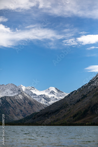 landscape with mountains, green trees and blue lake on a cloudy sky background Altai