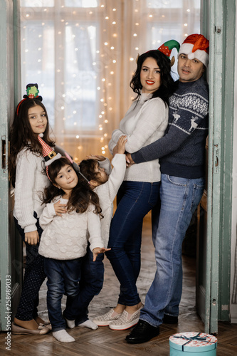 Funny parents and their three little daughters stand in the room with Christmas decor