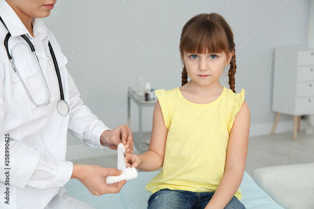 Female doctor applying bandage on little girl's finger in clinic. First aid Female doctor applying bandage on little girl's finger in clinic. First aid