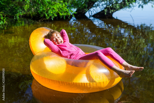 Little girl relaxes in an inflatable chair, floating on the water. © mihakonceptcorn