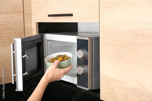 Young woman using microwave oven in kitchen