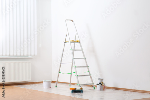 Stepladder and painting tools near wall in empty room