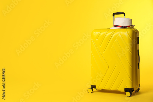 Bright suitcase with hat on color background. Space for text