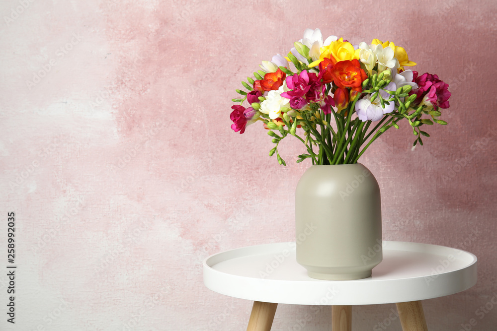 Bouquet of spring freesia flowers in vase on table against color background, space for text Bouquet of spring freesia flowers in vase on table against color background, space for text