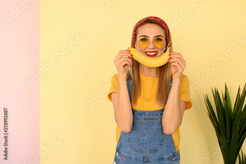 Positive young smiled girl with open banana on yellow and pink background. Smile, happy concept