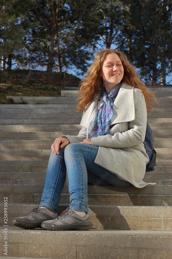 red-haired woman in a coat enjoying the spring sunshine