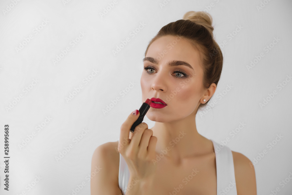 Beautiful young women with red lipstick in her hand indoor on white background. Beauty, make up, red lipstick concept. Close up Beautiful young women with red lipstick in her hand indoor on white background. Beauty, make up, red lipstick concept. Close up