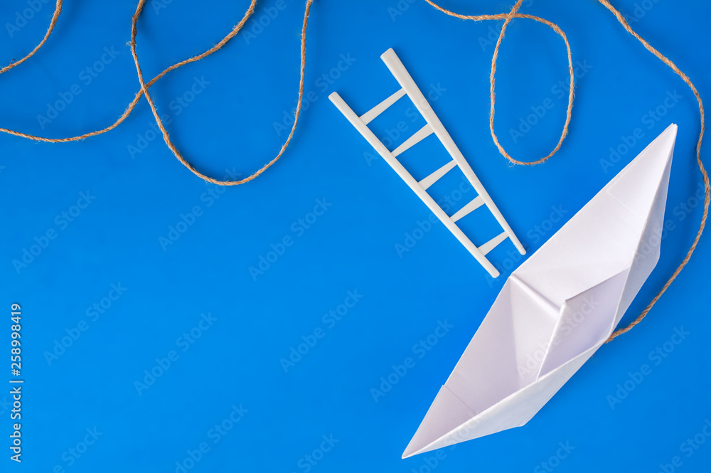 White paper boat with a white ladder and a piece of rope on a blue background