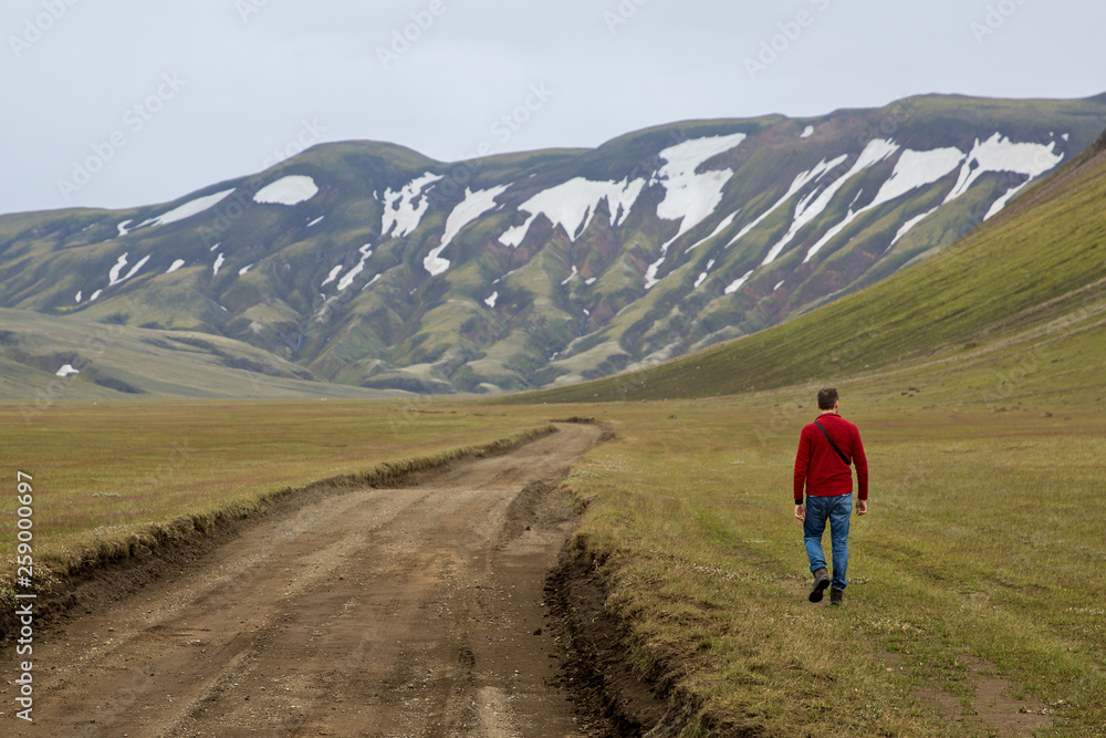 A man walks against the rugged green slopes of the volcanic hills