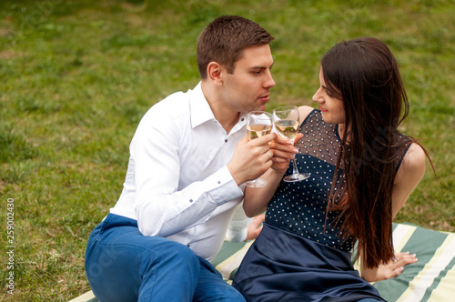Close up photo of romantic couple in love drinking wine and looking to each other on green grass background