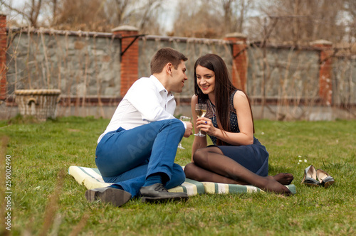 Young couple in love sitting on a picnic blanket in a park, drinking wine